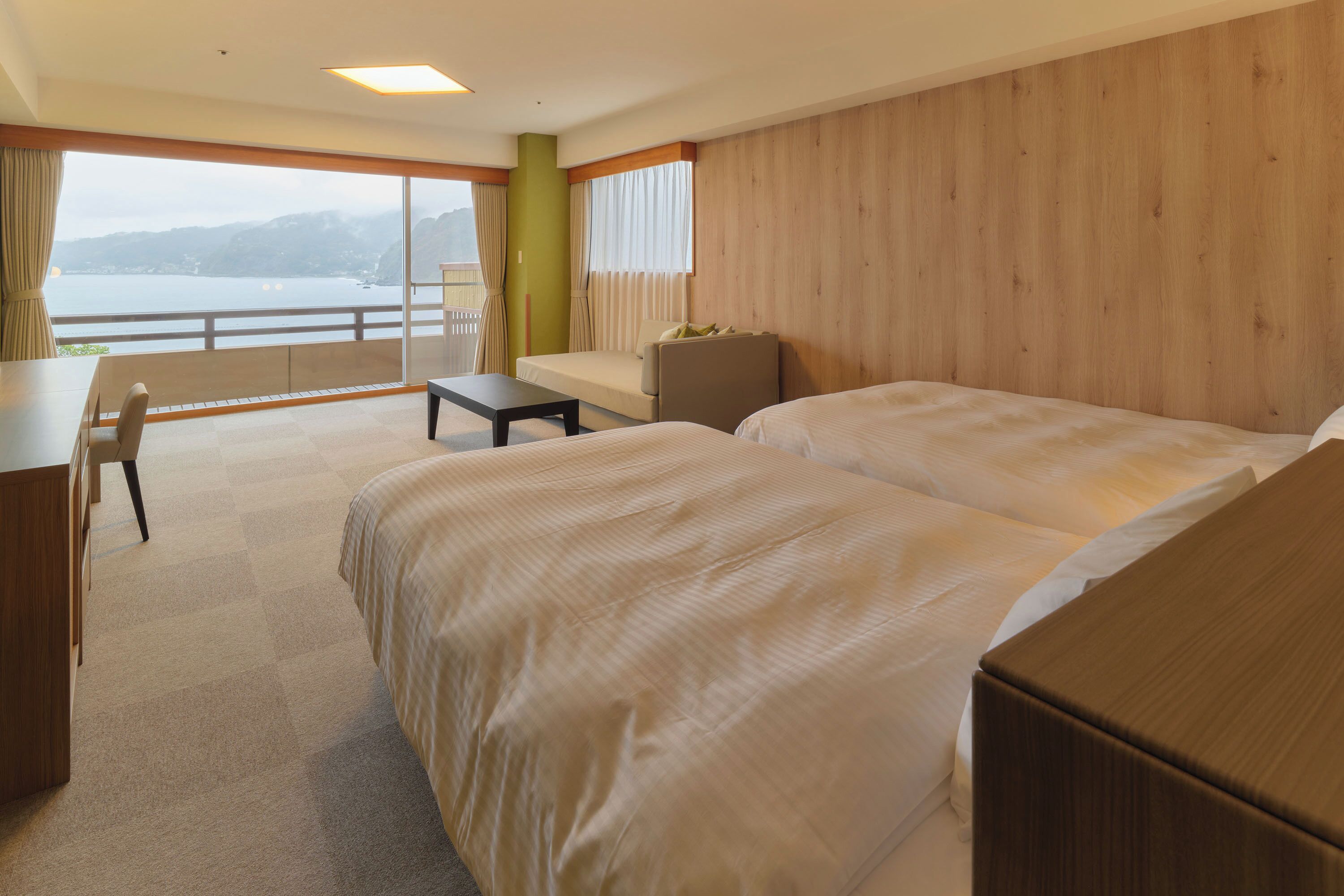 A hotel room with two beds, a desk, a chair, and a view of the water.