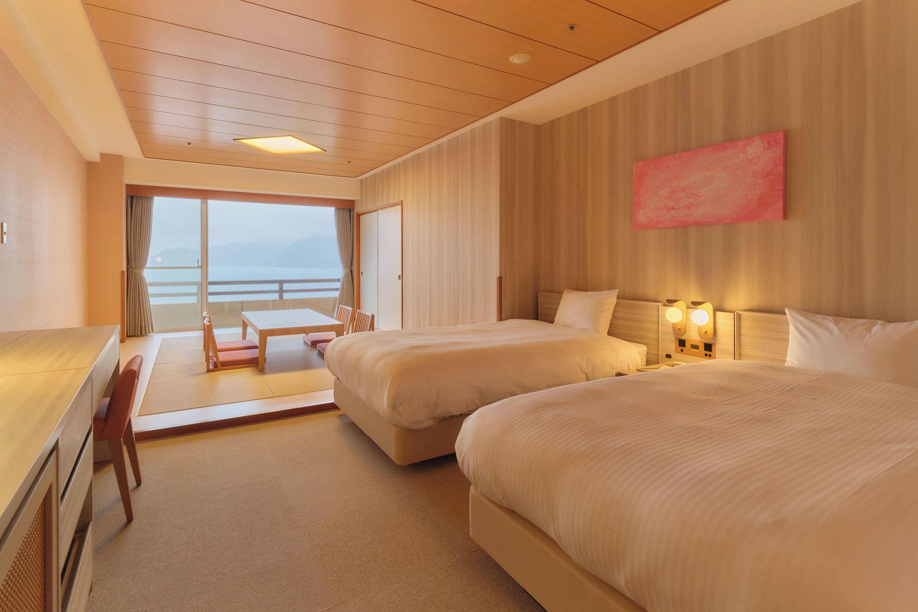 Habitación de hotel con dos camas, un escritorio, una silla, una mesa y vista al mar.