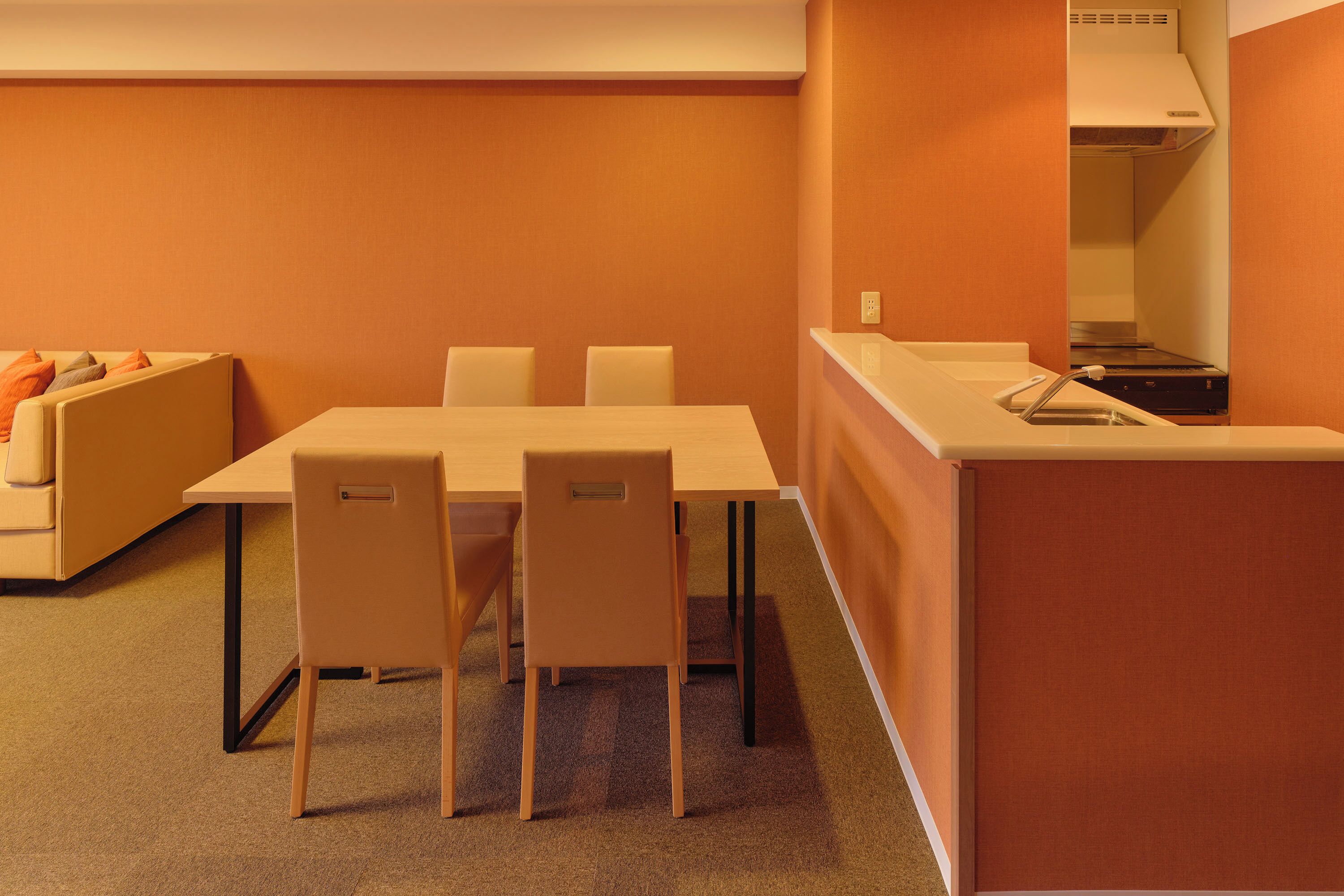 A conference room with a table, chairs, a sofa, and a kitchenette area.