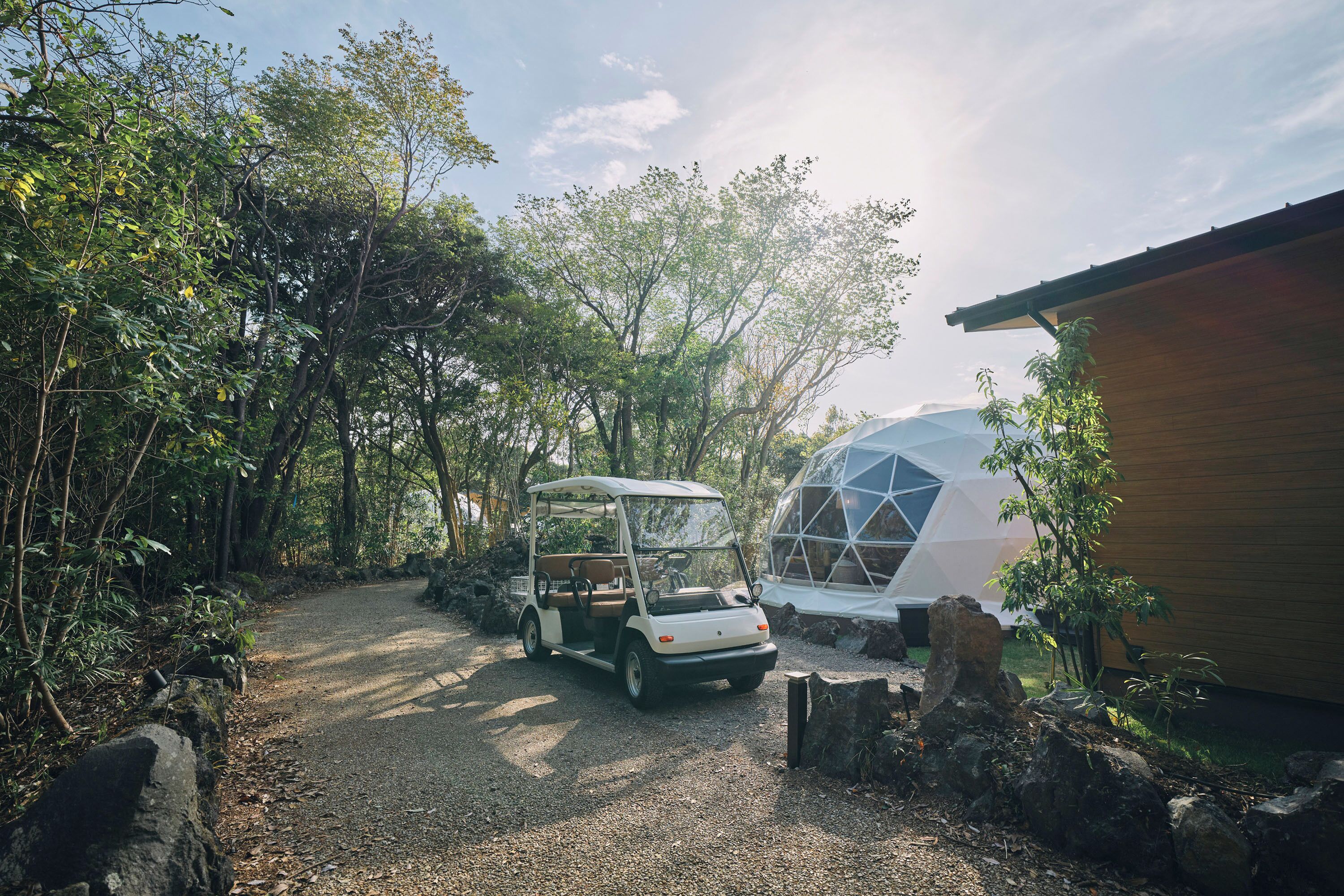 A golf cart parked on a gravel path, a geodesic dome structure, and a wooden building.