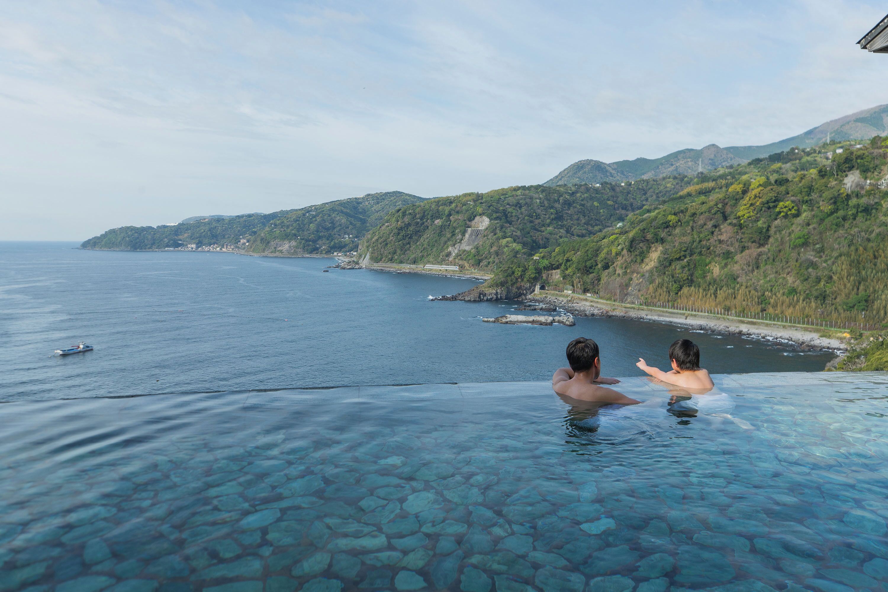 A couple in a clear infinity pool with a view of the sea and hills.