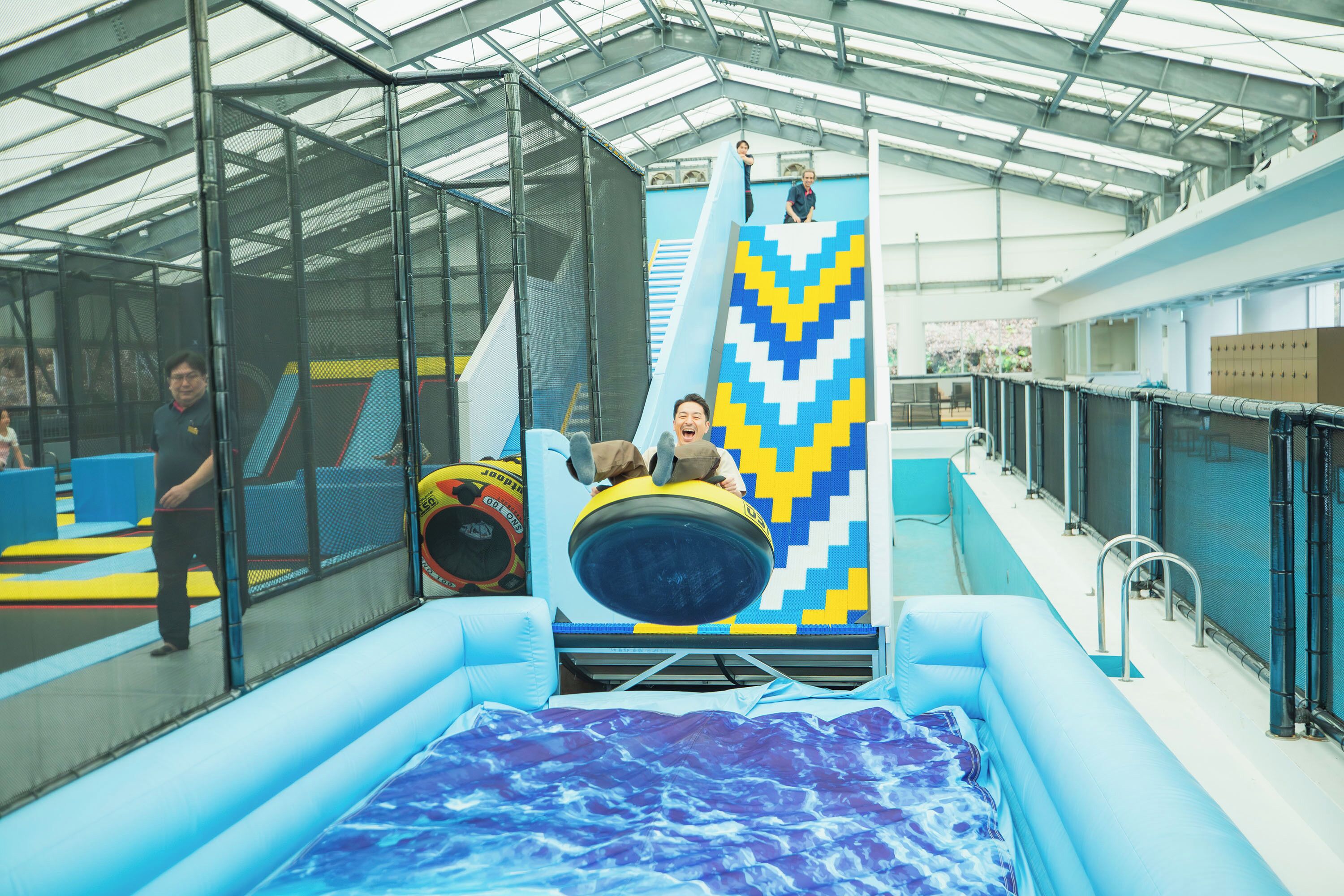 An indoor water slide with a blue and yellow chevron design, surrounded by inflatable walls and a pool.