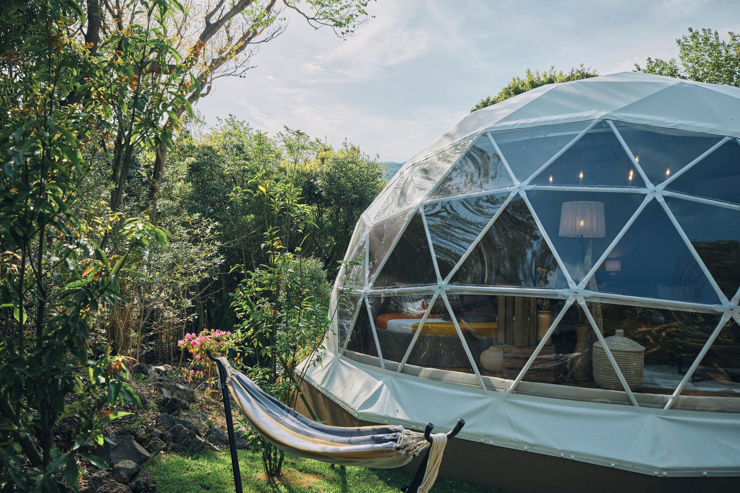 Une structure en forme de dôme géodésique, avec un hamac et des plantes en pot au premier plan.