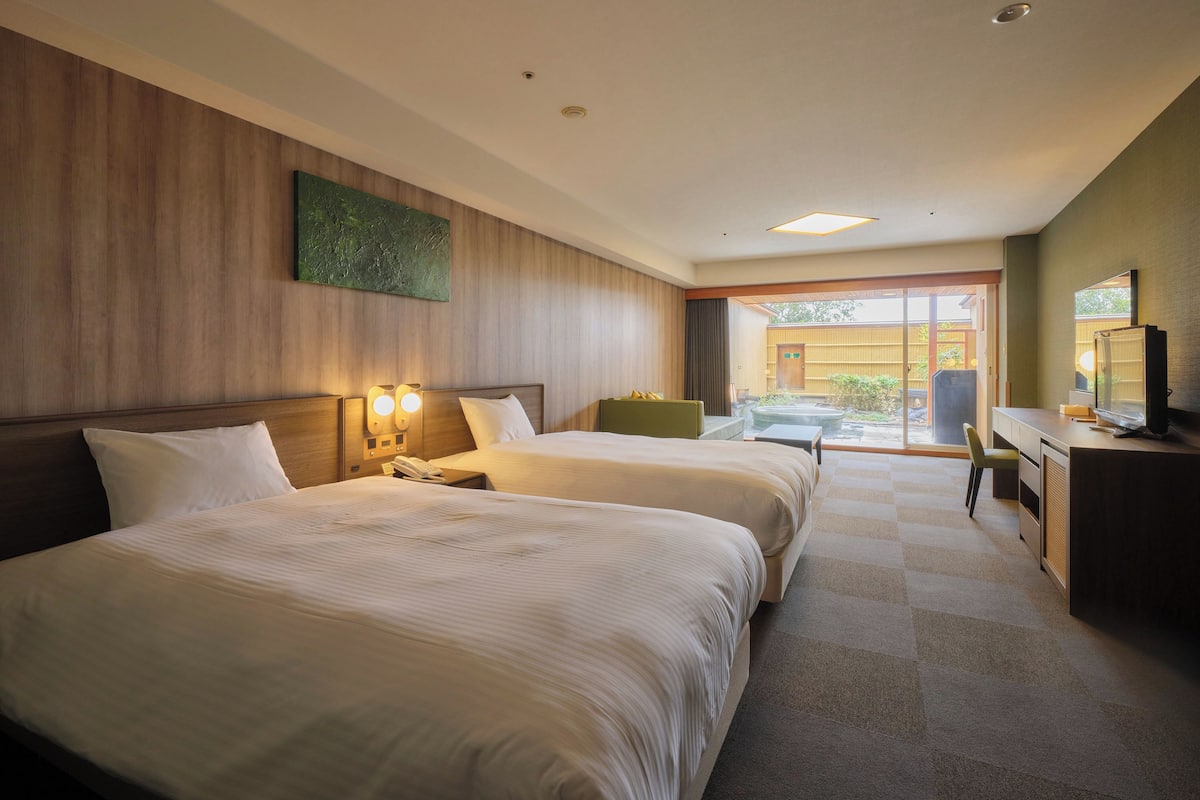 A hotel room with two beds, a desk, a chair, a television, and a view of the outside.