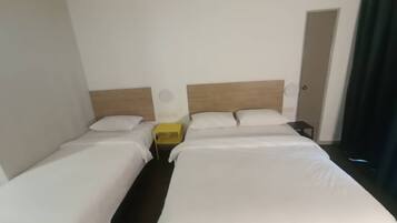 Habitación de hotel con dos camas individuales, cabecero de madera, mesita de noche con un objeto amarillo y una puerta a la derecha.