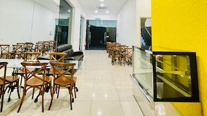 A spacious indoor area with multiple tables and chairs, a glass partition, and a yellow accent wall. - Big Tree Hotel  (Temerloh)