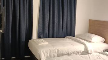 Quarto de hotel com duas camas, cortinas escuras, cabeceira de madeira e piso de madeira.