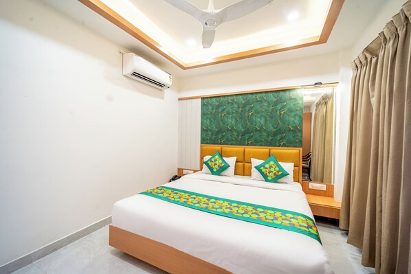 A hotel room with a bed, a ceiling fan, an air conditioning unit, a green patterned headboard, and a window with curtains. - Treebo Lotus Blue (Bhopal)