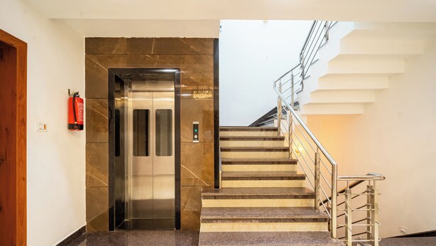 A modern elevator with a marble finish, a staircase with metal railings, and a fire extinguisher mounted on the wall. - Treebo Lotus Blue (Bhopal)