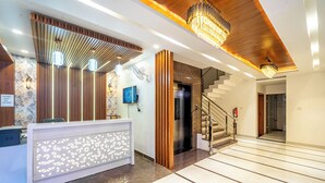 A modern reception area with a wooden reception desk, a staircase, and a chandelier. - Treebo Lotus Blue (Bhopal)