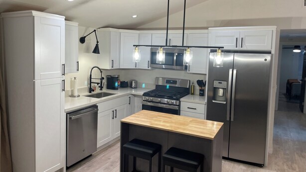 Una cucina moderna con mobili bianchi, elettrodomestici in acciaio inossidabile, un'isola in legno con sgabelli e illuminazione a sospensione.