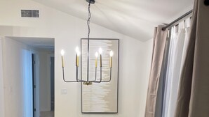Zona pranzo con tavolo rotondo circondato da sei sedie, un lampadario e un grande quadro astratto appeso al muro.
