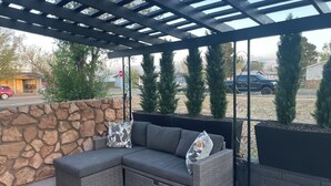 Un'area patio riparata con un muro in pietra, un divano componibile e alberi sempreverdi in vaso.