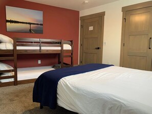 A hotel room with a bunk bed, a single bed, a painting on the wall, and wooden doors.