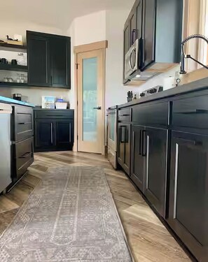 A kitchen with dark cabinets, a patterned rug, and a microwave above the counter.