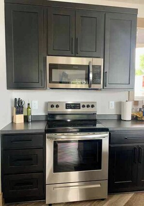 A kitchen with dark cabinets, a stainless steel microwave, and an oven.