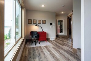 A hallway with a desk, a lamp, and framed pictures on the wall.