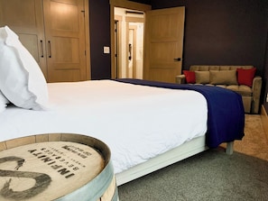 A bedroom with a bed, a wooden wardrobe, a sofa, and a small table with a barrel.
