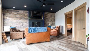 Ein modernes Wohnzimmer mit Steinwand, Ledersofas, Kamin und Deckenventilator.