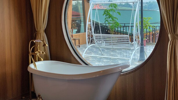 A bathroom with a round mirror, a bathtub, and a view of a balcony with outdoor furniture and plants. - Alley House (Sa Pa)