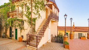 Ein Gebäude mit einer Treppe, die zu einem Balkon führt, umgeben von Kopfsteinpflaster und Blumentöpfen.