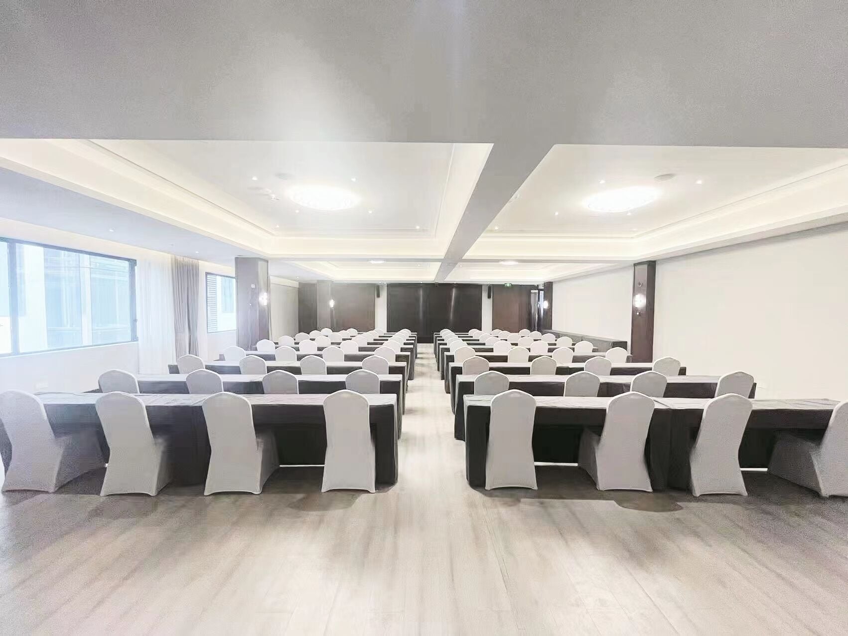 A conference room with rows of tables and chairs, large windows, and a modern ceiling design.