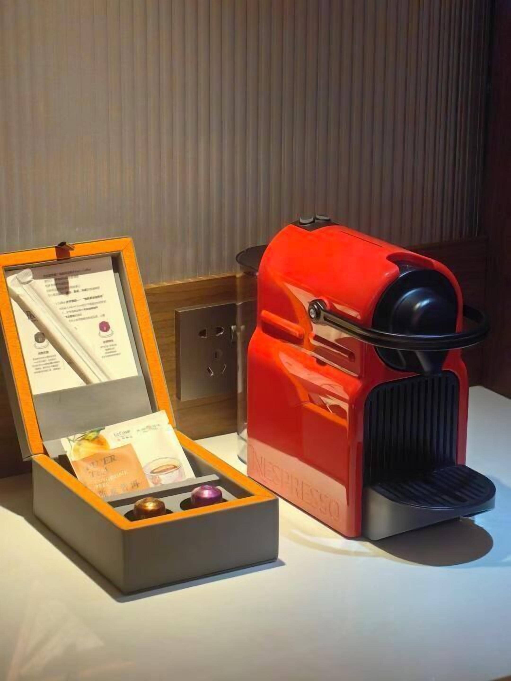 A red Nespresso machine next to a wooden box containing a menu and a small purple item.