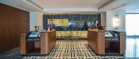 Een hotel receptie met twee receptionisten achter bureaus voorzien van digitale kiosken.