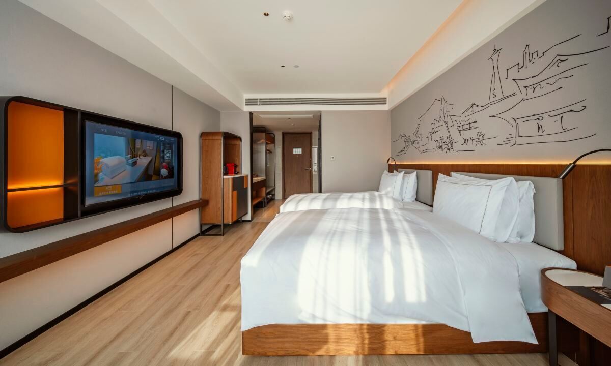 Una habitación de hotel moderna con una cama grande, un televisor montado en la pared y un cabecero de madera.
