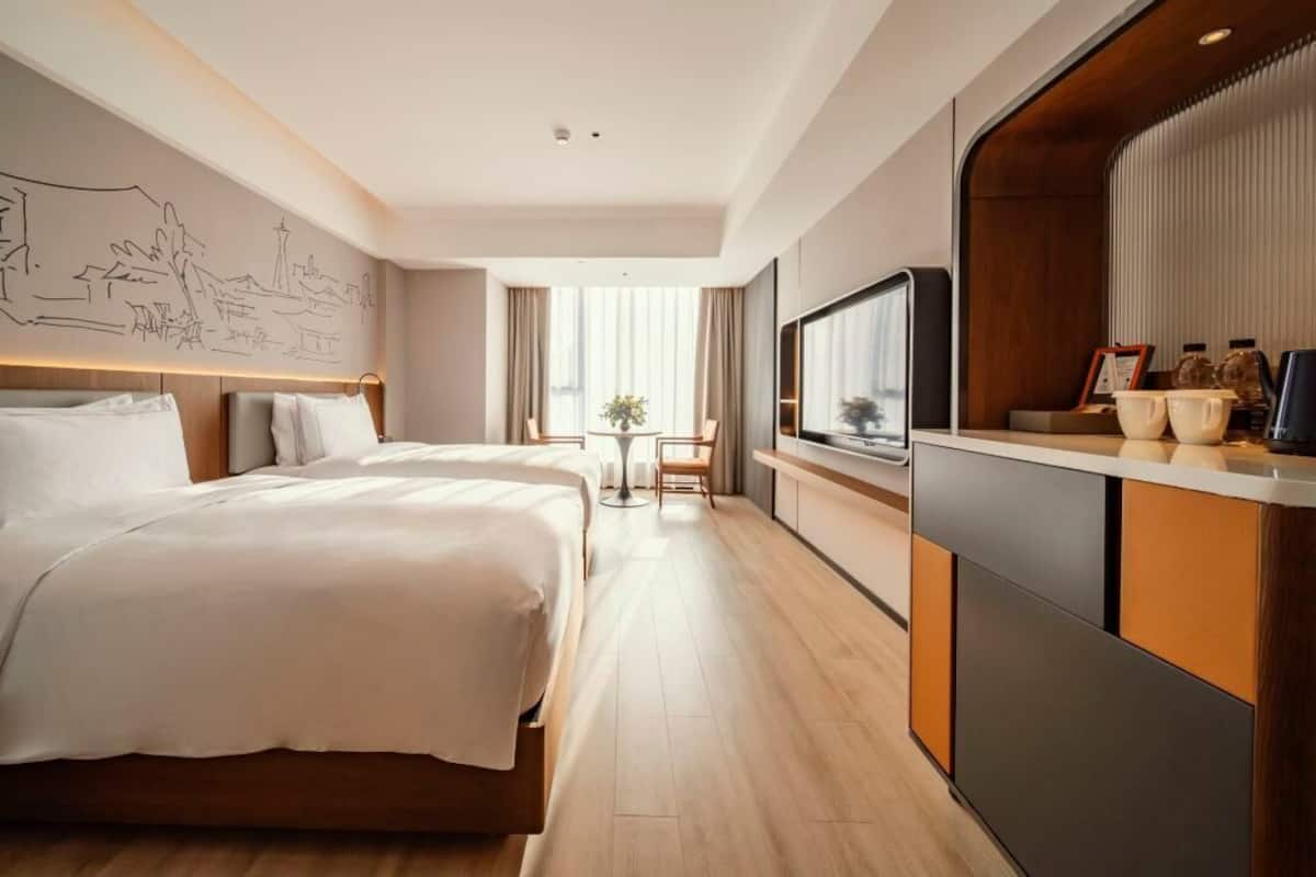Een hotelkamer met een groot bed, een bureau met een televisie, en een muur met een stadsgezicht muurschildering.