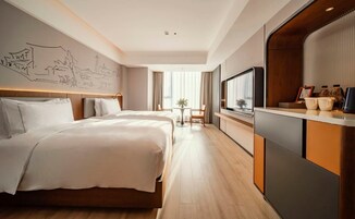 Habitación de hotel con una cama grande, un escritorio con televisor y una pared con un mural de paisaje urbano.