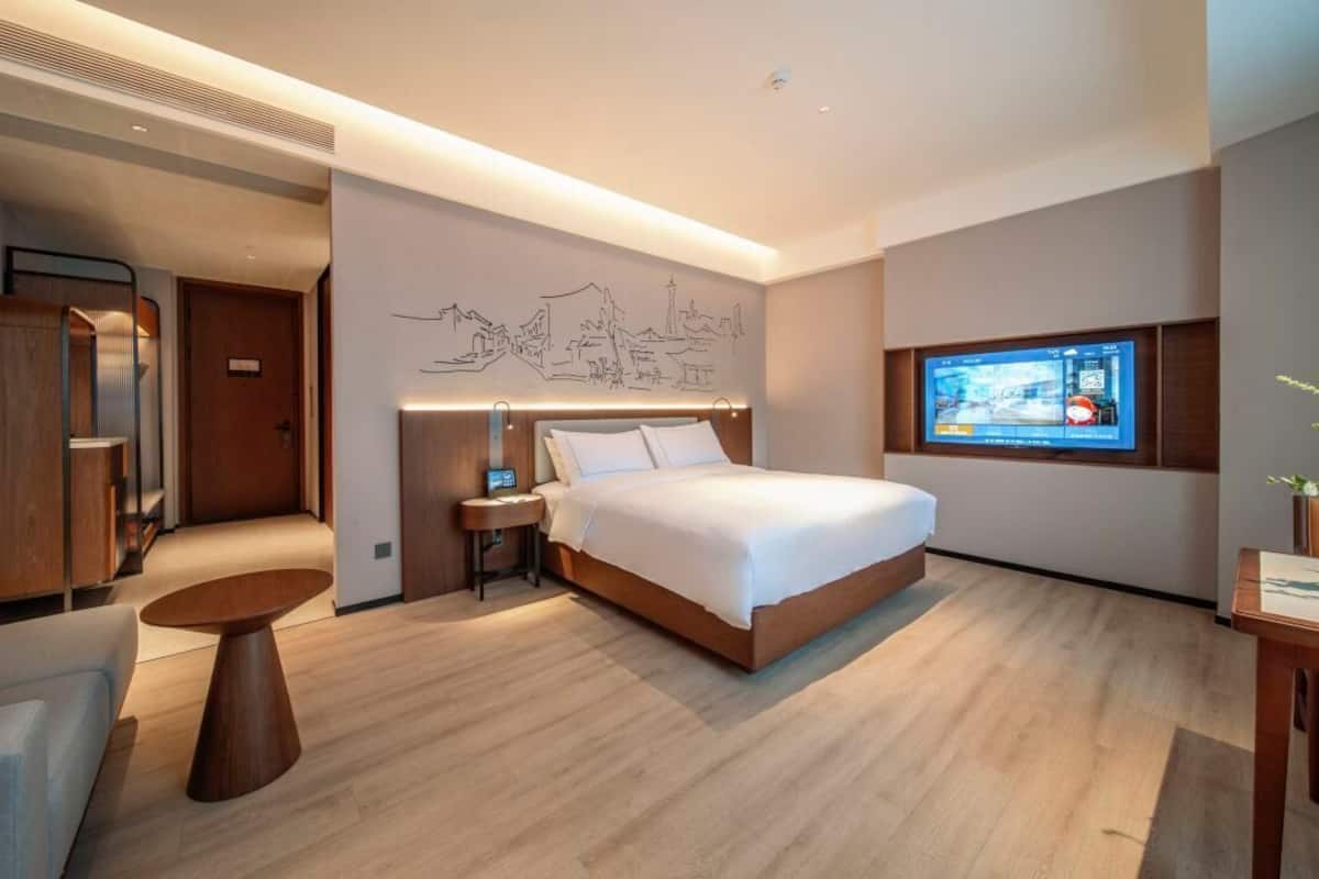 Een moderne hotelkamer met een groot bed, een aan de muur bevestigde televisie en een houten vloer.