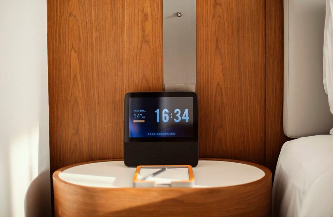 Een digitale klok op een nachtkastje in een hotelkamer.