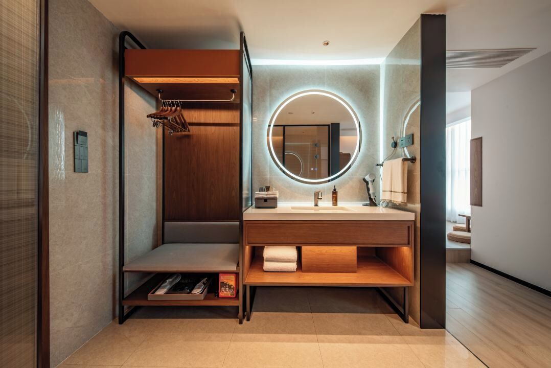 Un baño moderno con tocador de madera, un espejo redondo y una zona de ducha integrada.