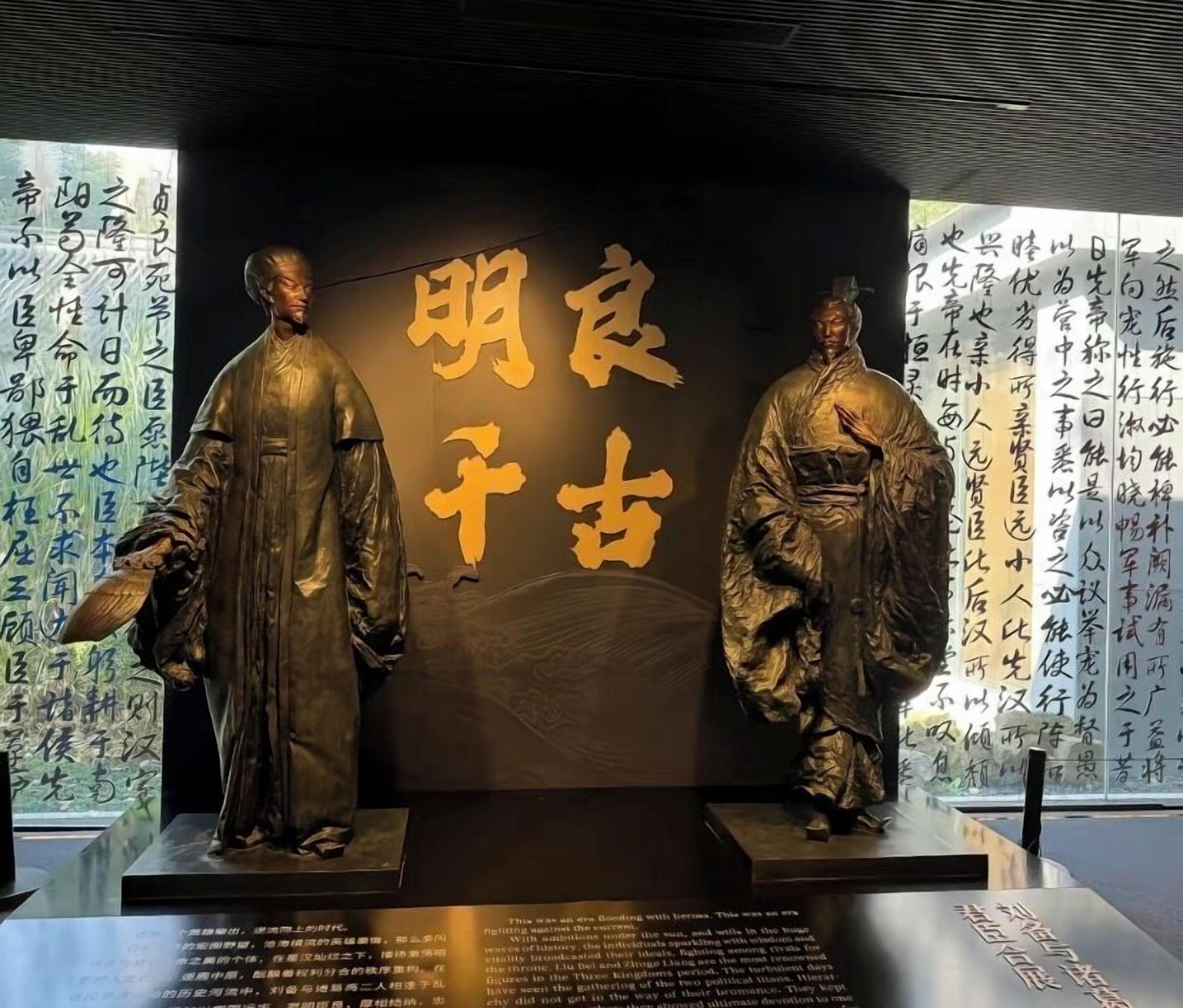 A display of two bronze statues with inscriptions in Chinese characters, set against a backdrop with additional text.