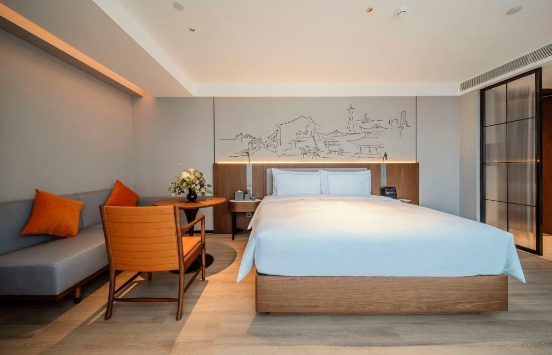 Een moderne hotelkamer met een groot bed, een slaapbank, een klein tafeltje en een decoratieve muurschildering.