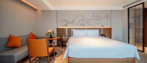 A modern hotel room with a large bed, a sofa, a small table, and a decorative wall mural.