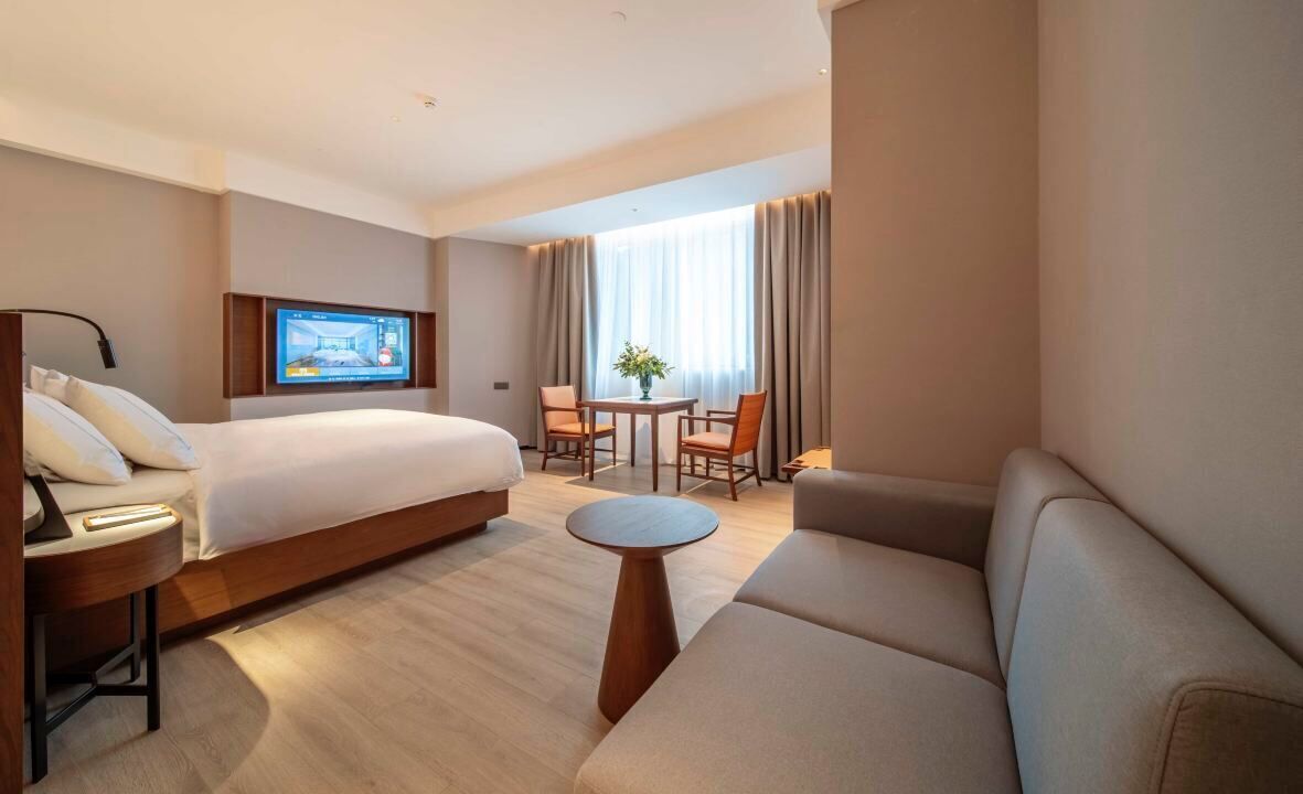 A hotel room with a bed, a sofa, a small table, and a TV mounted on the wall.
