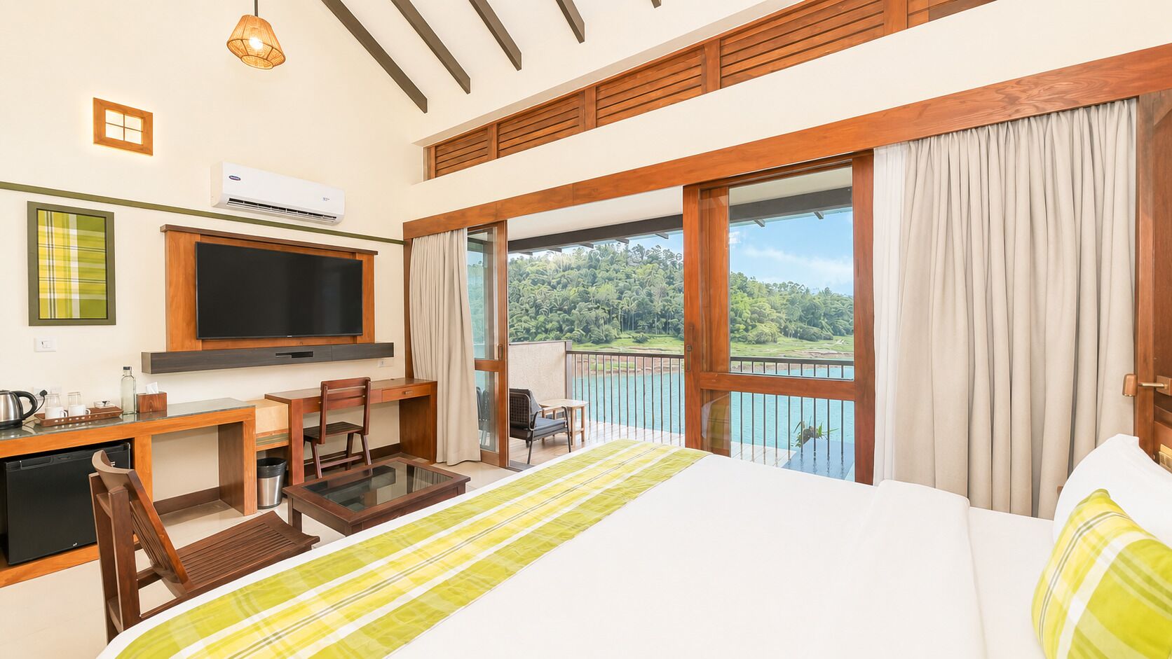 A hotel room with a bed, a desk with a chair, a television, and a balcony with a view of the outdoors.