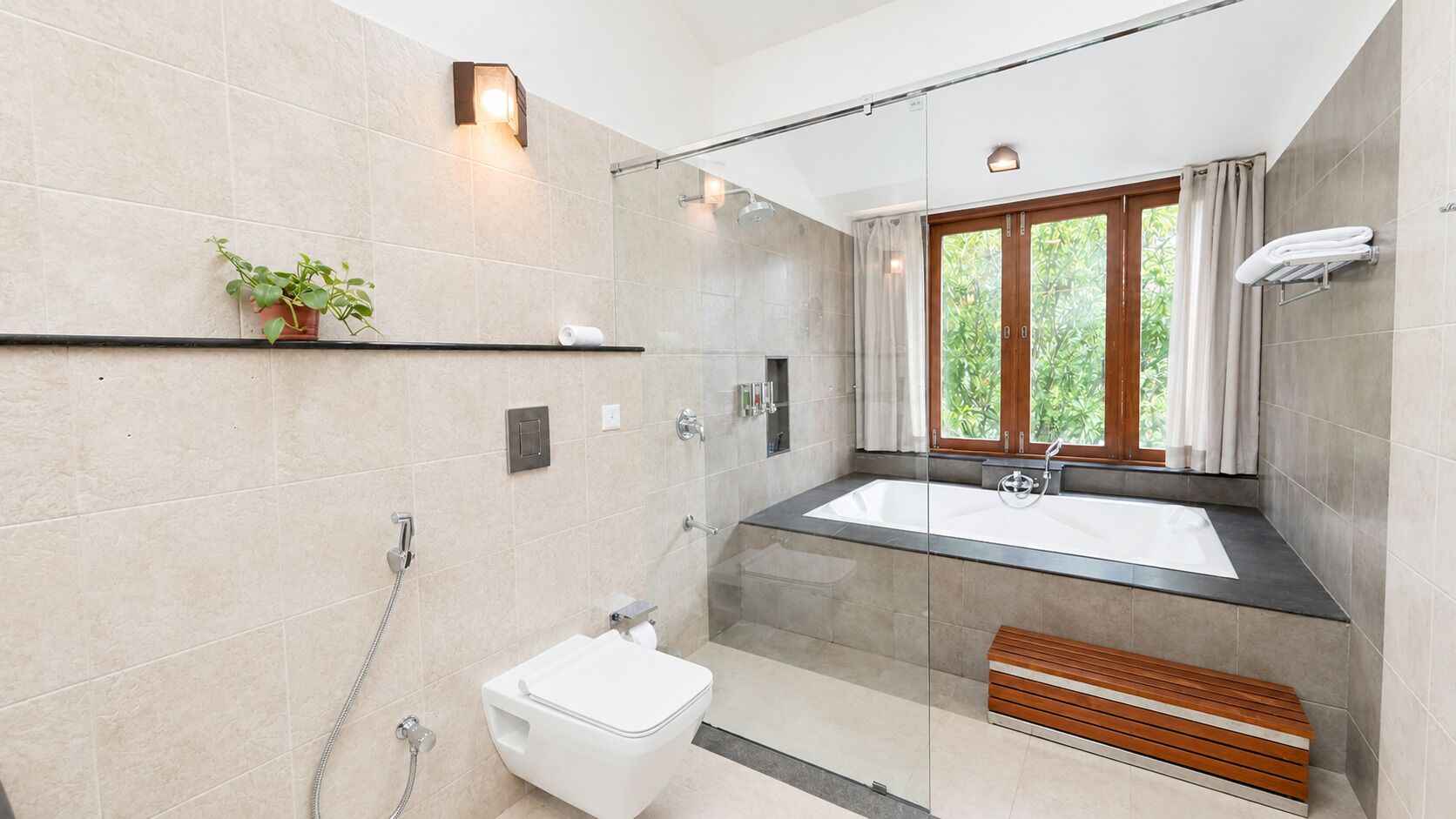 A modern bathroom with a glass-enclosed shower, a white toilet, a large bathtub, and a wooden bench.