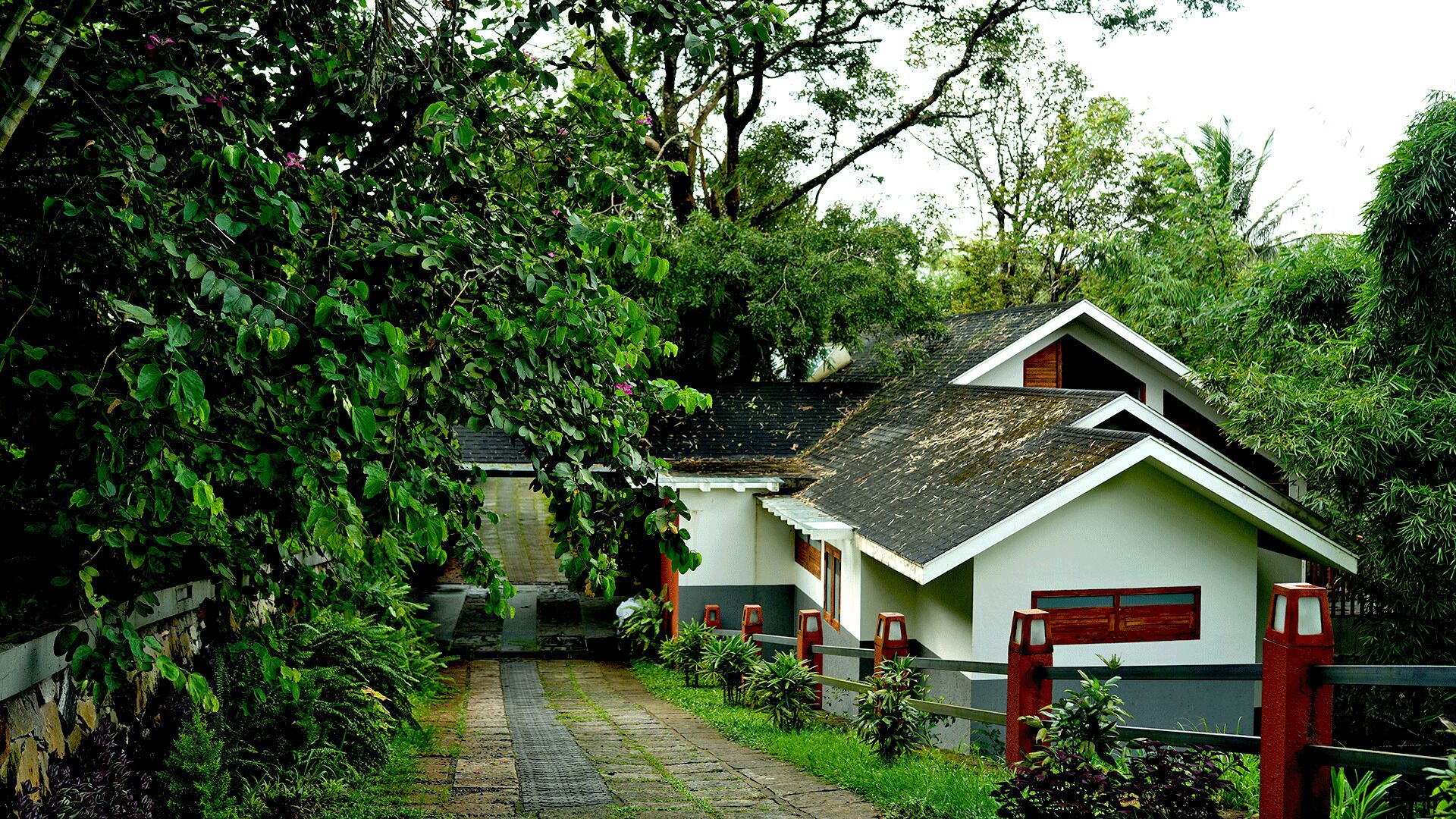 A row of traditional-style cottages with sloped roofs, surrounded by lush greenery and a stone pathway leading to the entrance.