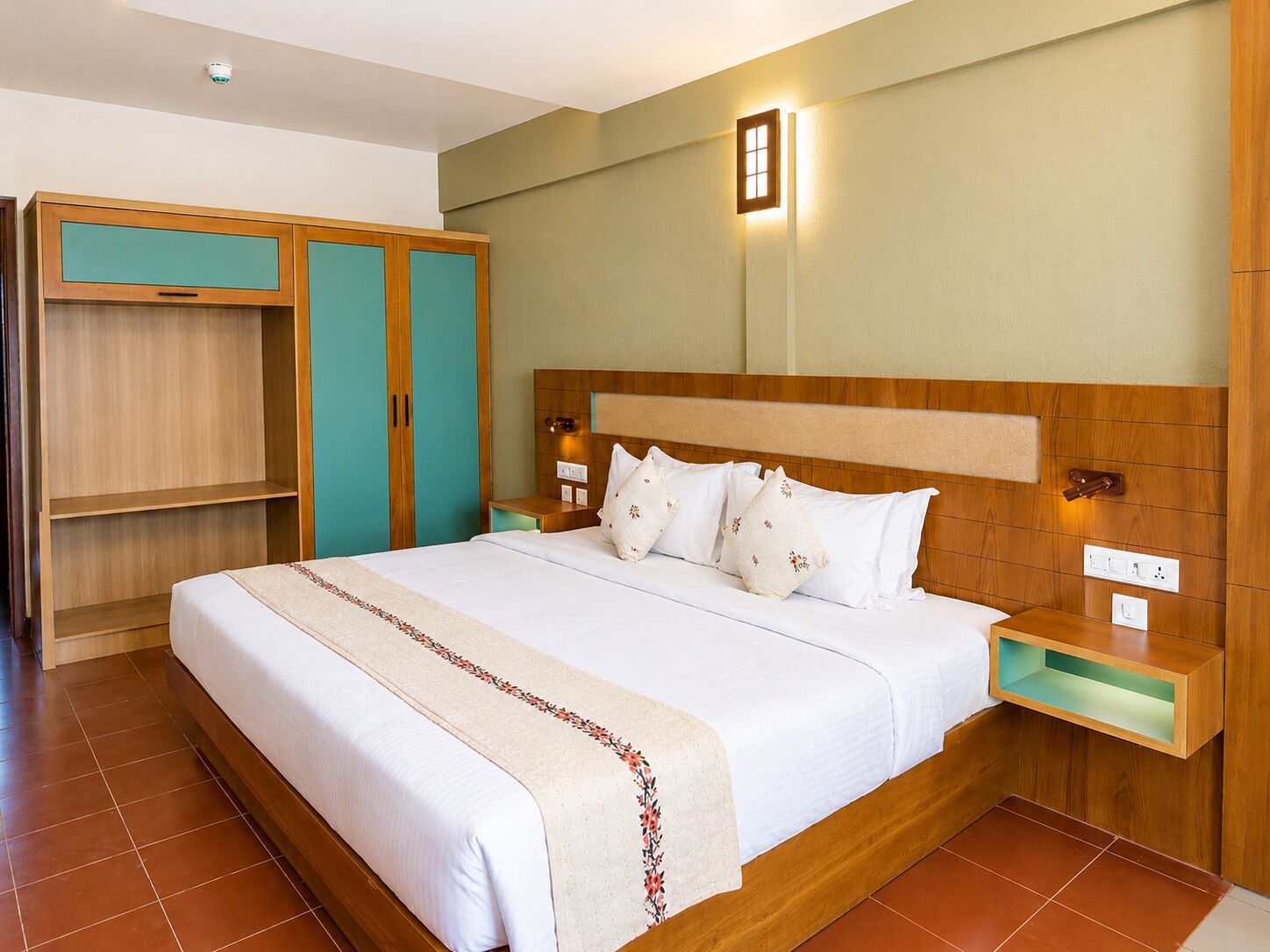 Habitació d'hotel amb llit, una petita taula de nit, armari i una làmpada penjada a la paret.