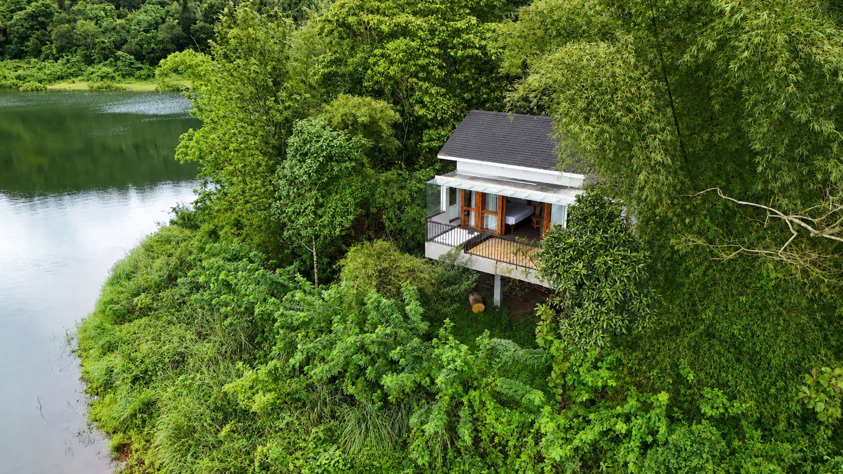 Una casa con balcón que da a un lago, rodeada de abundante vegetación.