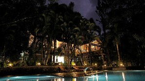 A nighttime view of a resort with a swimming pool, palm trees, and a building with illuminated windows. - Wayanad Silverwoods Forest Resort & Spa (Vythiri)