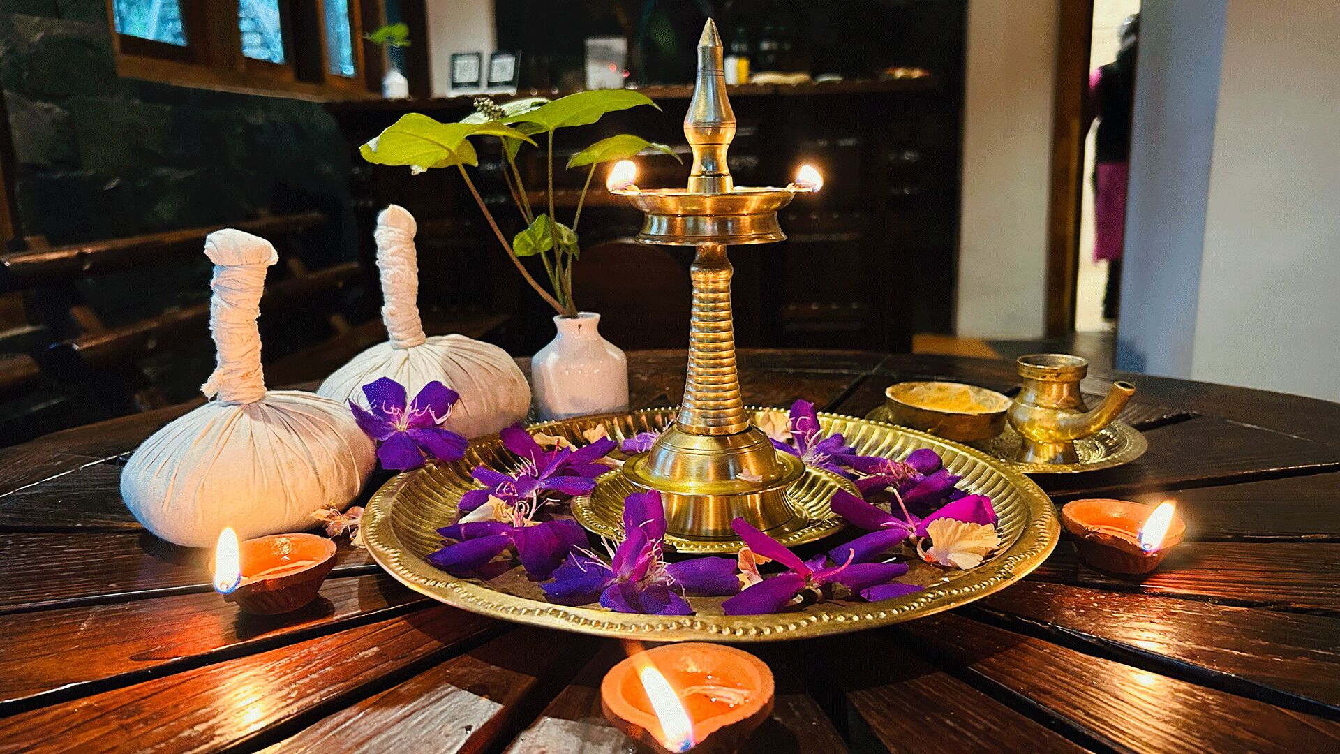 Uma mesa com uma lâmpada de latão, velas e flores.