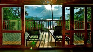 A wooden deck with two chairs and a table, overlooking a body of water and mountains. - Wayanad Silverwoods Forest Resort & Spa (Vythiri)