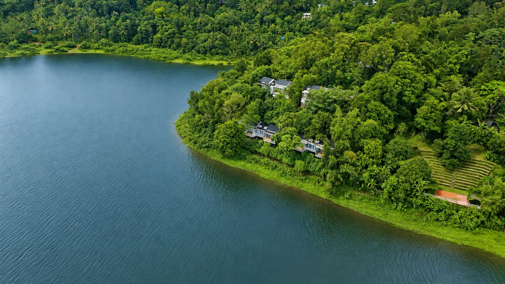A lakeside property with a house surrounded by dense greenery.