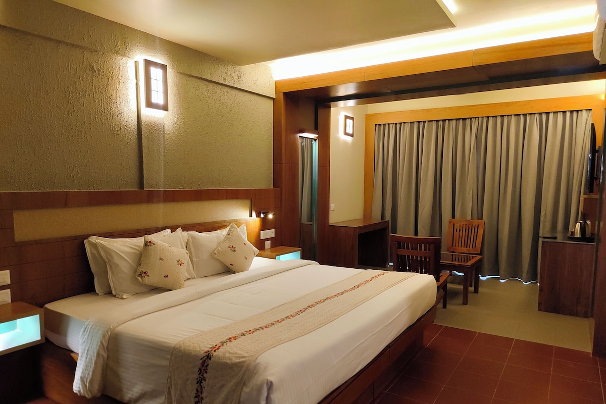 A hotel room with a large bed, a desk, a chair, a television, and a window with curtains.