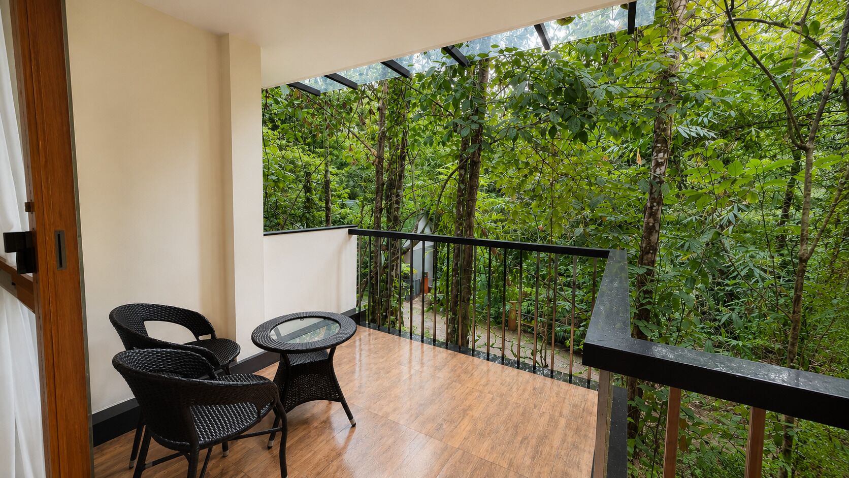 Ein Balkon mit Holzboden, zwei Korbstühle, einem kleinen runden Tisch und Blick auf einen  üppigen grünen Wald.