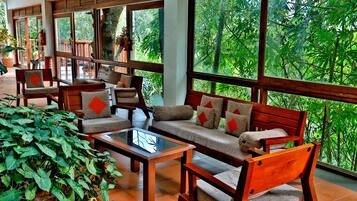 A spacious indoor area with wooden furniture, large windows, and lush greenery outside.